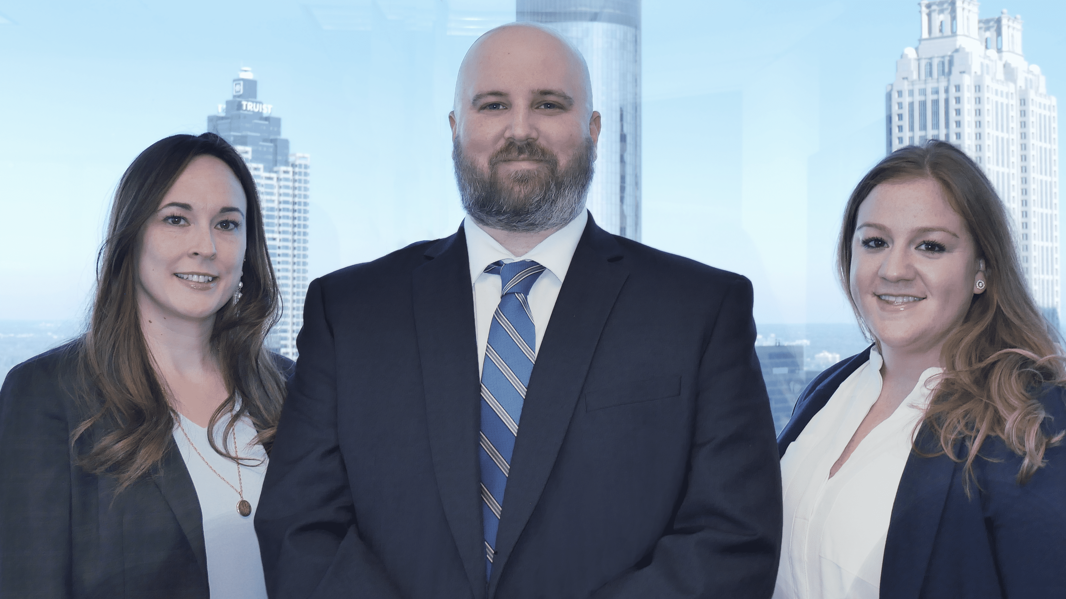 Attorneys Tom Church and Whitney Baker standing in front of the Atlanta skyline with paralegal Emily Brooks